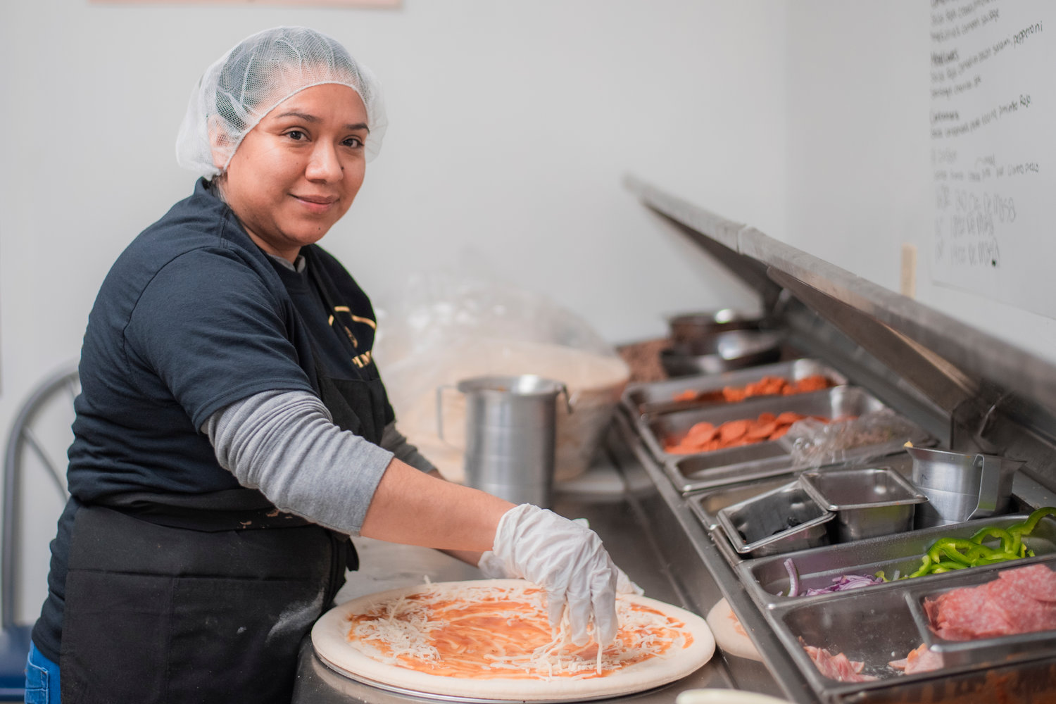 Karla Villegas smiles while stacking cheese and prepping orders at Pizza Mia in Tenino.