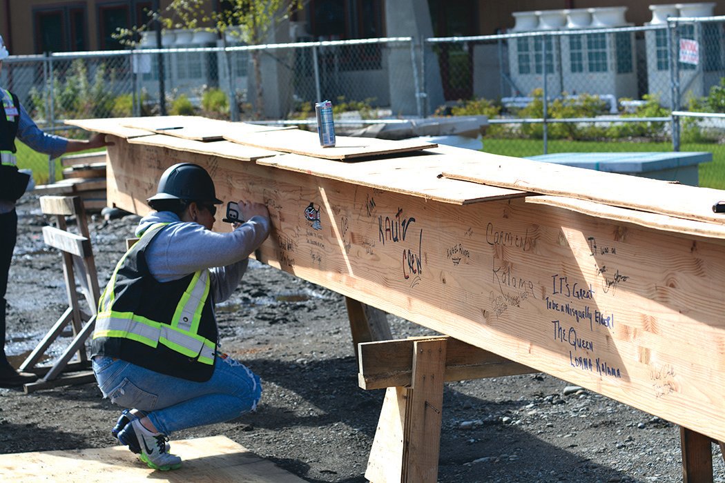 a worker at the Elder Center construction site signs the wood pillar that was ceremoniously lifted onto the building.