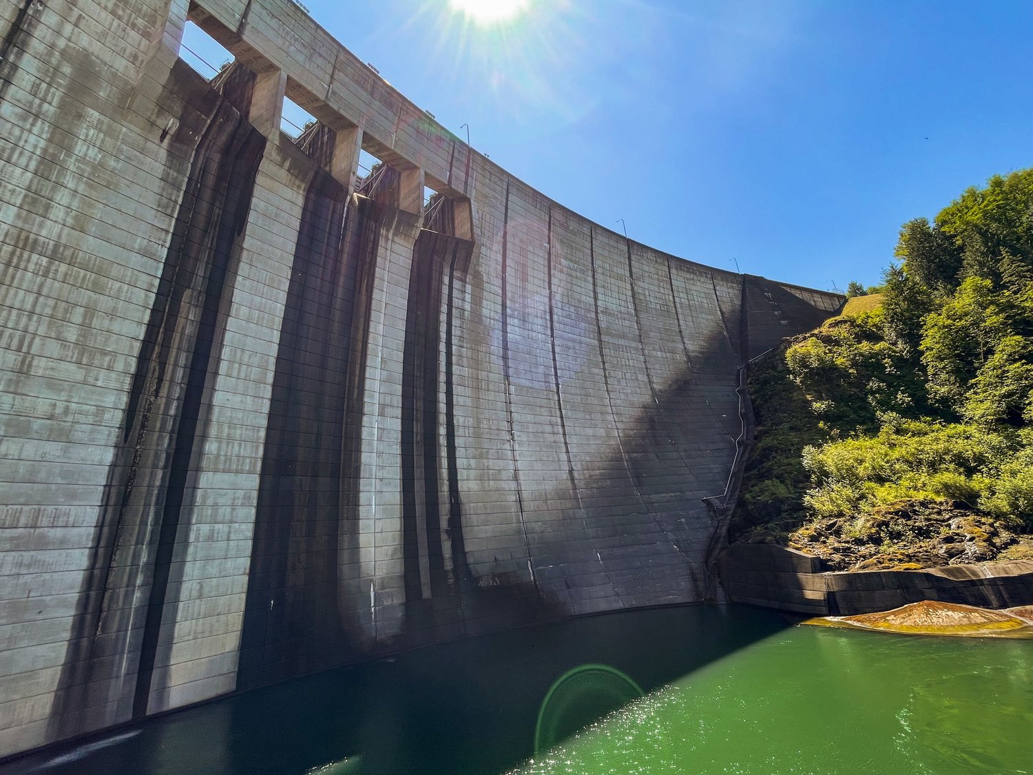 The sun shines down on the Mossyrock Dam casting a shadow on the water.
