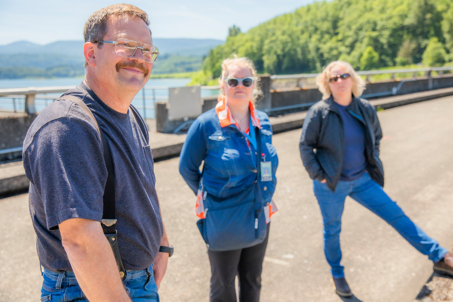 Clarence Lupo smiles and looks on from atop the Mossyrock Dam alongside Monika Sundbaum and Kyrra Wilson.