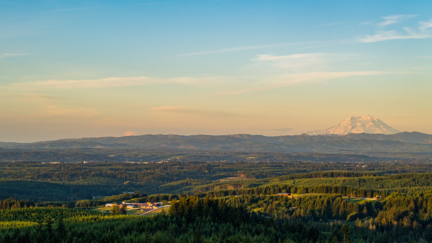 The sky glows a hazy peach color over Mount Rainier as the sun begins to set on the summer solstice, seen from Crego Hill in Adna.