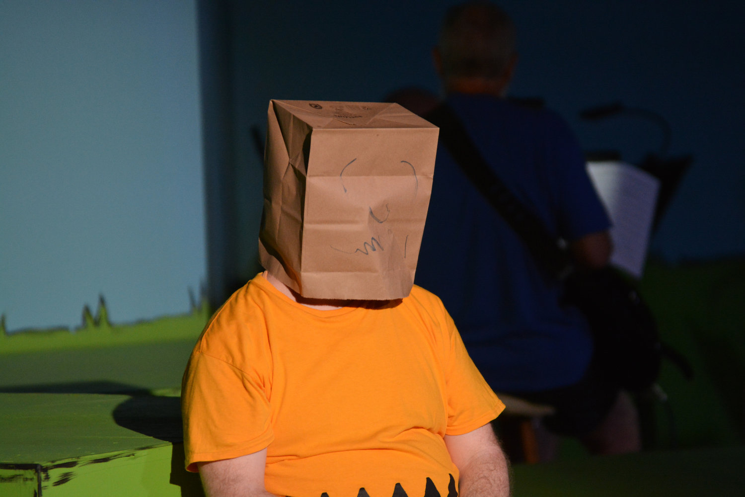 The actor portraying Charlie Brown wears a brown paper bag over his head, after another embarrassing attempt to talk to the “cute girl at lunch.”