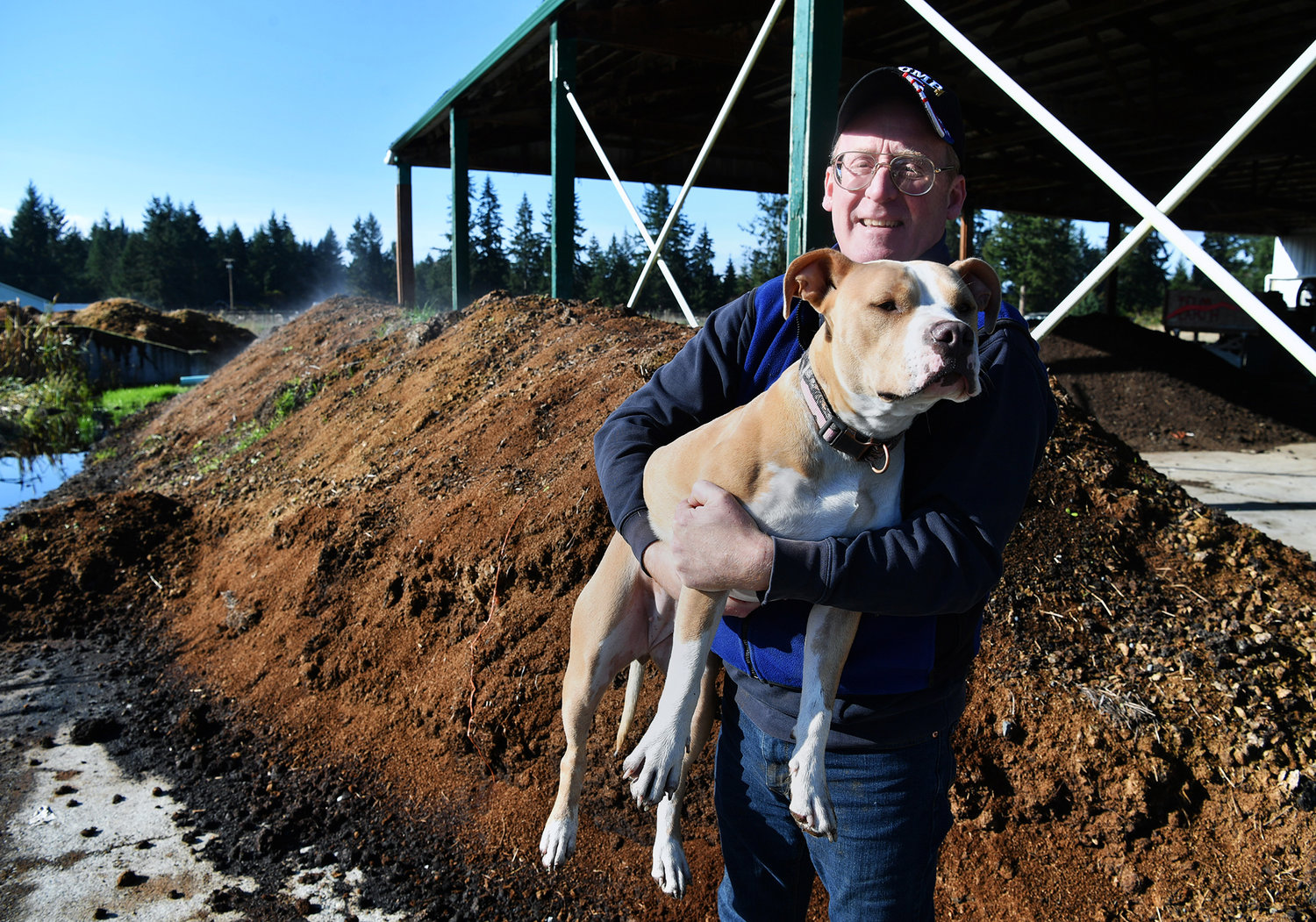 Kelan Moynagh, the owner of Yelm Earthworm and Castings Farm, holds his dog, Princess, next to a berm of worm castings derived from horse manure in this file photo from 2020.