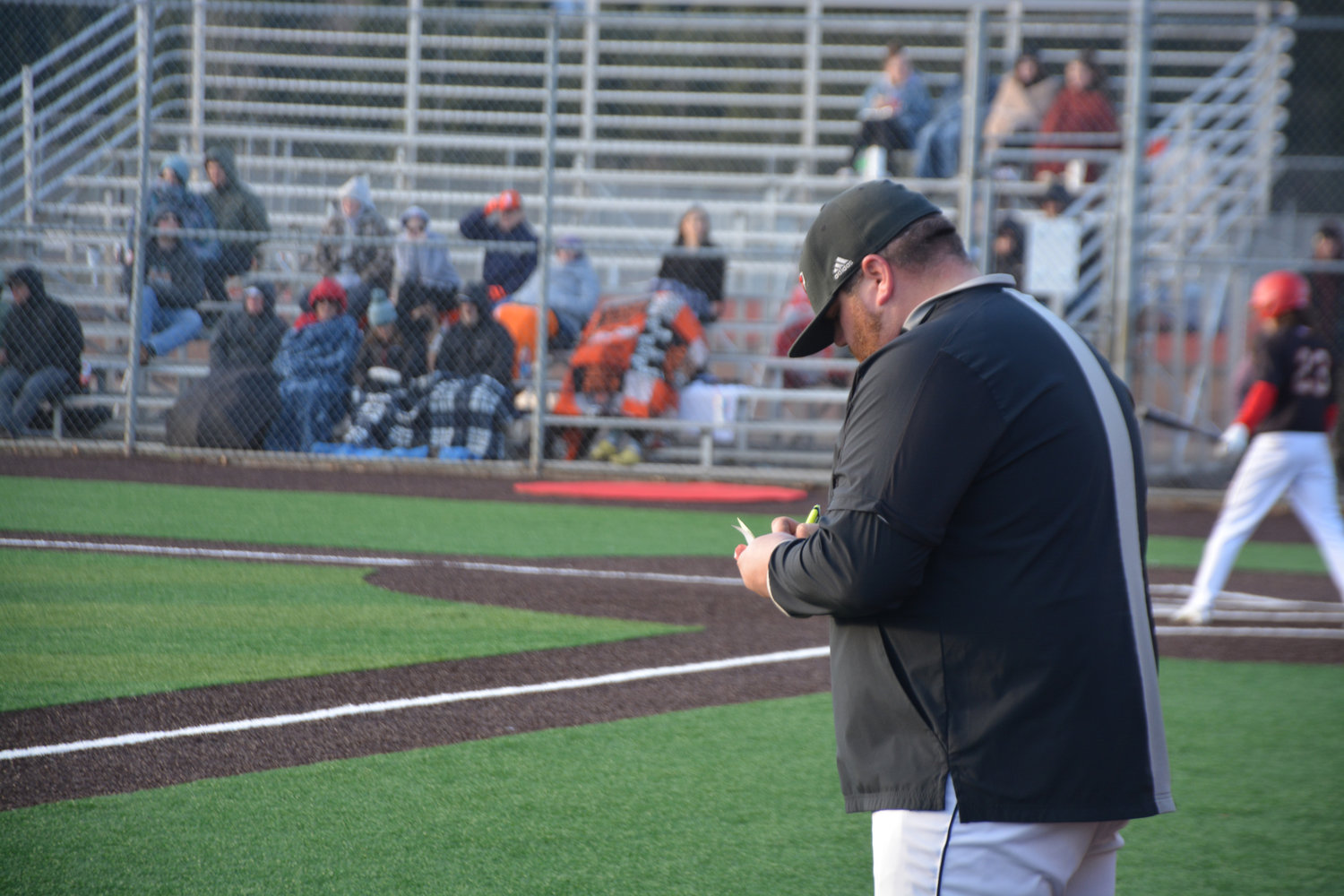 Yelm Head Coach Zach Miller takes notes as one of his players awaits a pitch during a game against Rainier on Friday, March 10.