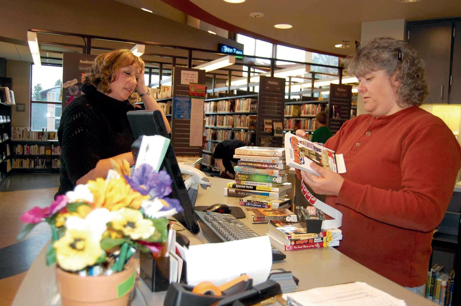Linda Davis of Yelm, left, asks library aide Jody Renu a question after checking out a stack of library books in this file photo.