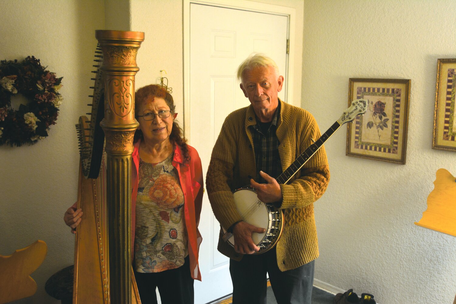 Roy residents Roxie and Bob Goodwin stand with their instruments, a harp and banjo, respectively, in their home on Oct. 24.